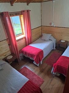 Habitación con 2 camas y ventana con cortinas rojas. en Cabañas Robinson en Puerto Puyuhuapi
