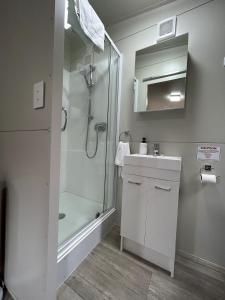 a white bathroom with a shower and a sink at Takapuna Beach Holiday Park in Auckland