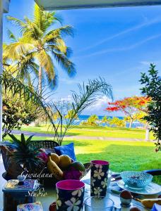 a table with food and a view of a palm tree at Accès Direct Plage, Magnifique Vue Mer, Les Gwada Studios, Village Vacances in Sainte-Anne
