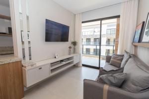 a living room with a couch and a tv on a wall at 139C - lindo apartamento a 50m da praia de Canto Grande in Bombas