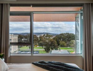 een slaapkamer met een groot raam met uitzicht op een park bij Jamieson Apartments Reid ACT in Canberra