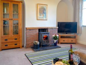 a living room with a brick fireplace and a television at Butterhole Cottage in Kelton