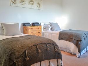 a bedroom with two beds and a wooden dresser at Butterhole Cottage in Kelton
