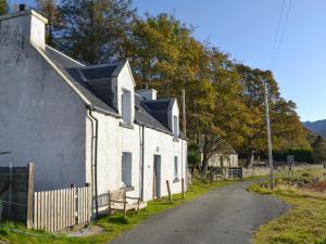 a white house with a bench next to a road at Shore Cottage in Arnisdale