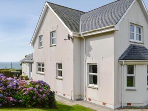 a white house with a black roof and purple flowers at Saffron in Portpatrick