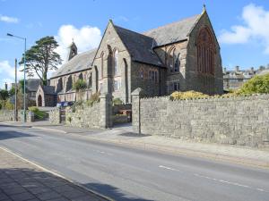 a church with a stone wall next to a street at Apartment 6 harlech in Criccieth