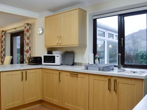 cocina con armarios de madera, microondas y ventana en Hoot House, en Abergynolwyn