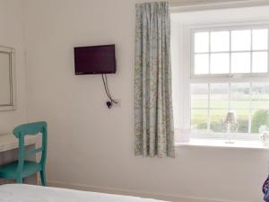 a bedroom with a window with a television and a green chair at Cheviot View in Beal