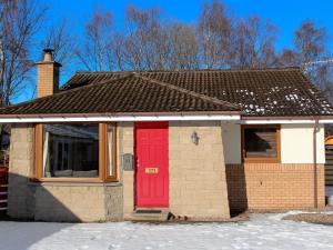a brick house with a red door in the snow at Holly Lodge in Aviemore