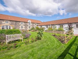 a garden with two benches in front of a building at Lucklaw Steading Cottage in Logie