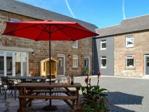 a picnic table with a red umbrella on a patio at Smithfield House in Tarbolton