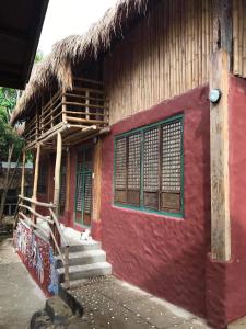 a red building with stairs and a thatch roof at Capiz Beach Villa family room for 6 pax in Calatagan