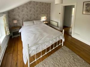 a bedroom with a white bed with a wooden floor at Honey Cottage in Friston