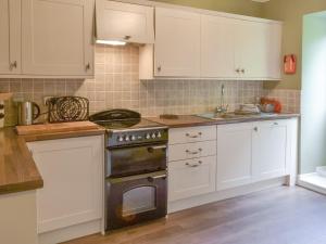 cocina con armarios blancos y horno en Prudhoe Mews, en Alnmouth