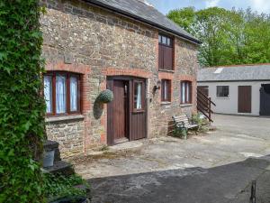 a brick house with a wooden door and a bench at The Old Coach House in Woolfardisworthy