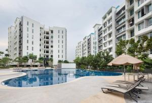 a swimming pool with chairs and an umbrella and some buildings at Midori Green By JK Home in Johor Bahru