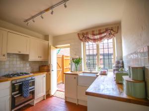 cocina con armarios blancos, fregadero y ventana en Dulcie Cottage en Benson