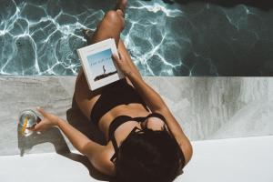 a woman in a bikini reading a book next to a pool at Bella Casa Noosa in Noosa Heads