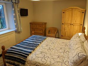 a bedroom with a bed and a dresser and a window at Drumlins Cottage in Gatebeck