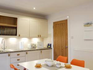 a kitchen with white cabinets and a table with orange chairs at Rhunahaorine Cottage in Gortinanane
