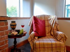 Butterhole Farmhouse في Kelton: كرسي مع وسادة حمراء وكأس من النبيذ