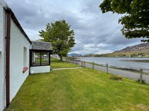 a house with a grassy yard next to a body of water at Lag Cottage in Dornie