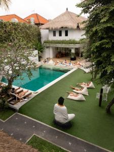 a group of people sitting on the grass by a pool at Puri Garden Hotel & Hostel in Ubud