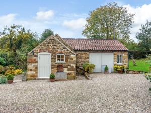 a stone cottage with white garage doors on a gravel driveway at Wren Cottage in Sutton