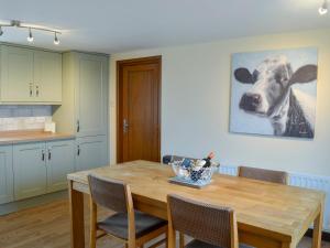 uma cozinha com uma mesa de madeira e uma pintura de vaca na parede em Seascape em Craster