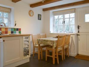 een keuken met een tafel, stoelen en ramen bij Quarrymans Cottage in Linkinhorne