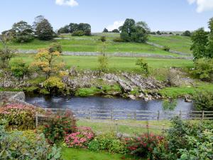 a view of a garden with a river and flowers at Inglenook Cottage in Grassington