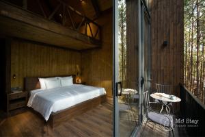 a bedroom with a bed and a balcony with a glass door at Mơ Stay - Forest Resort in Da Lat