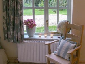a window sill with a chair and a vase of flowers at Honeysuckle Cottage in Oasby