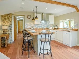 una cocina con armarios blancos y taburetes de bar en Stackyard Cottage, en Felmingham