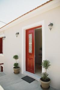 a red door on a white building with two potted plants at Rooms in Yard in Kórinthos