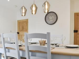 a dining table with white chairs and a clock on the wall at Sapphire Cottage in Pakefield