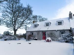 a house covered in snow with a red door at Garden Cottage in Tain