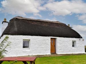a white building with a thatched roof with a wooden door at Taigh Violet Rose in Gramisdale