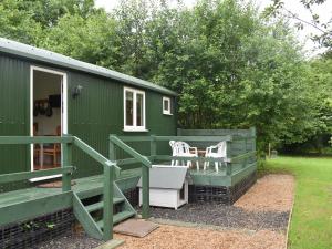 a green tiny house with a porch and two white chairs at Shepherds Hut 3 At Laddingford - Uk32532 in Yalding