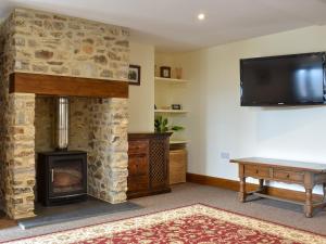 a living room with a stone fireplace and a flat screen tv at Bucknole Farm - The Old Shippon in Northleigh