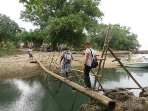 zwei Personen, die eine Holzbrücke über einen Fluss überqueren in der Unterkunft Nawori Sea View Bungalows N tours Packages in Wortatcha