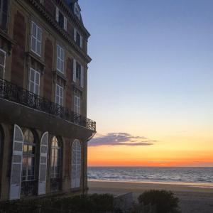 um edifício na praia com o pôr-do-sol ao fundo em Hotel Le Trouville em Trouville-sur-Mer