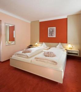 a bedroom with a large white bed with an orange wall at Vitalhotel Sonneck in Bad Wörishofen