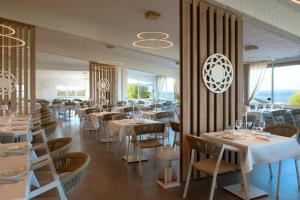 a restaurant with white tables and chairs and windows at AMASEA Resort in San Teodoro