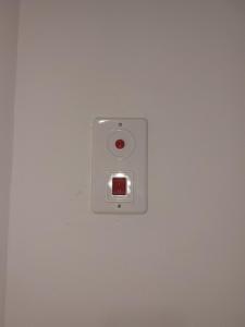 un interrupteur lumineux sur un mur blanc avec un bouton rouge dans l'établissement Sanny Bay, à Qiryat Yam