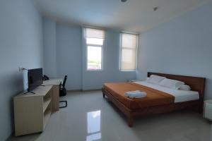 a bedroom with a bed and a desk with a television at Hotel Sutha Inn in Jambi
