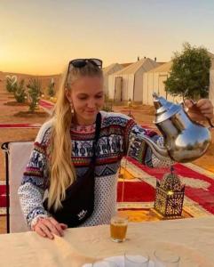 eine Frau sitzt mit einem Teekessel an einem Tisch in der Unterkunft Merzouga Nice luxury Camp in Merzouga