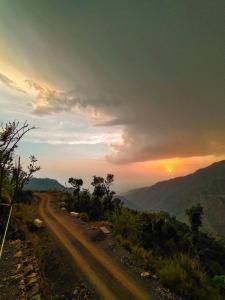 a dirt road with the sunset in the background at Shakoon Camps & Farmstay Nainital in Nainital