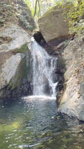 a waterfall on the side of a river with rocks at Shakoon Camps & Farmstay Nainital in Nainital