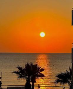 an orange sunset over the ocean with palm trees at Hai Hotel in Larnaca